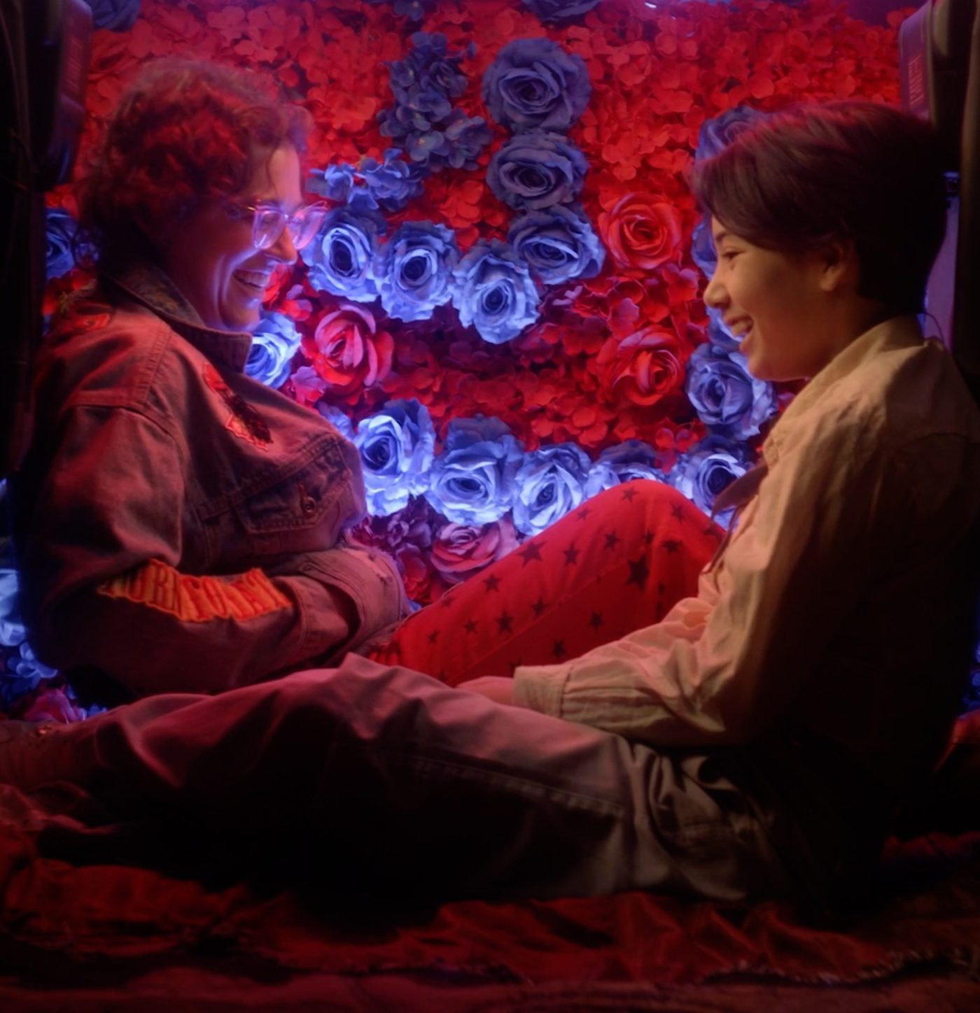 Two performers laughing on a stage of red and blue roses